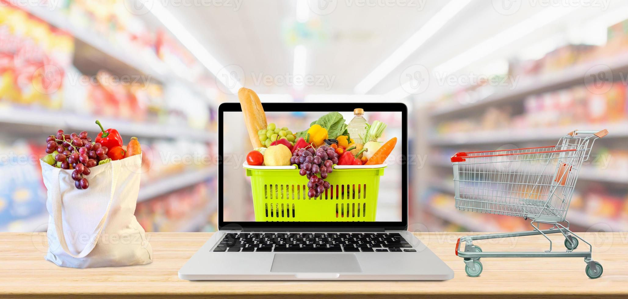 supermarket aisle blurred background with laptop computer and shopping cart on wood table grocery online concept photo