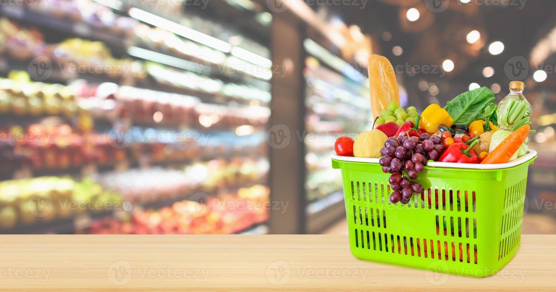 Shopping basket filled with fruits and vegetables on wood table with supermarket grocery store blurred defocused background with bokeh light photo