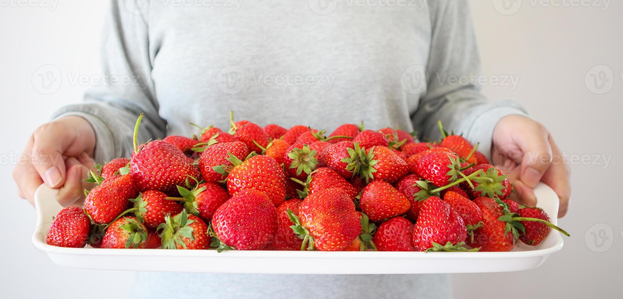 mujer sostenga una bandeja blanca con fresas rojas maduras foto