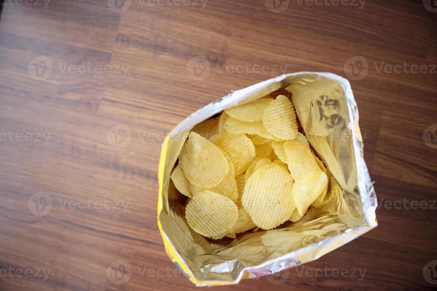 Potato chips in open snack bag close up on table floor photo