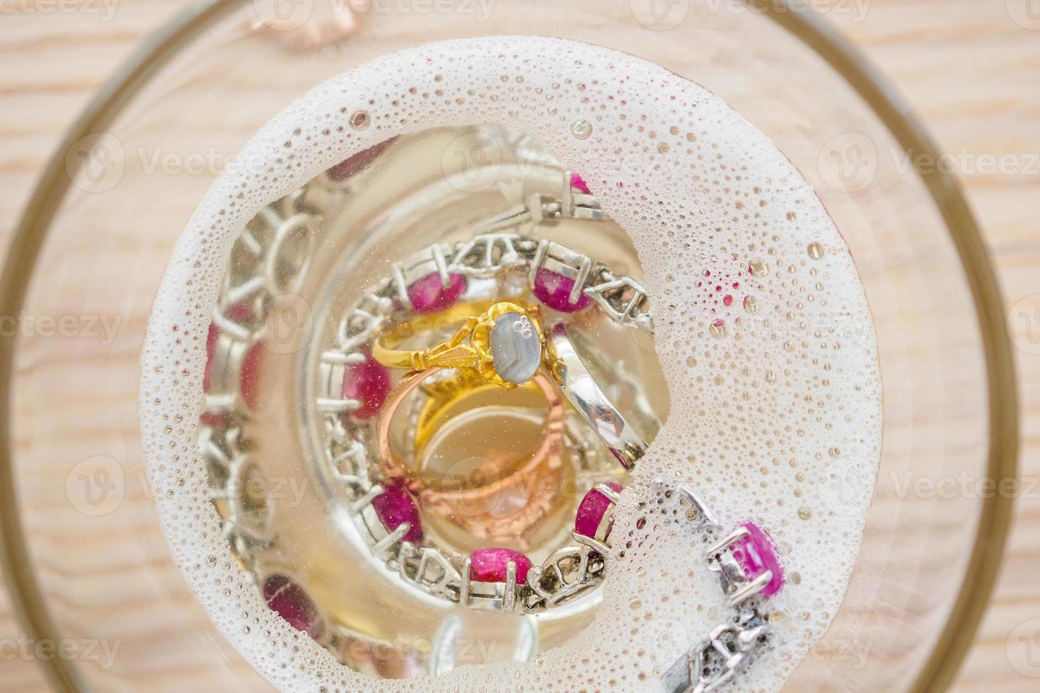 limpiar el anillo de diamantes de joyería vintage y la pulsera en vidrio sobre fondo de mesa de madera foto