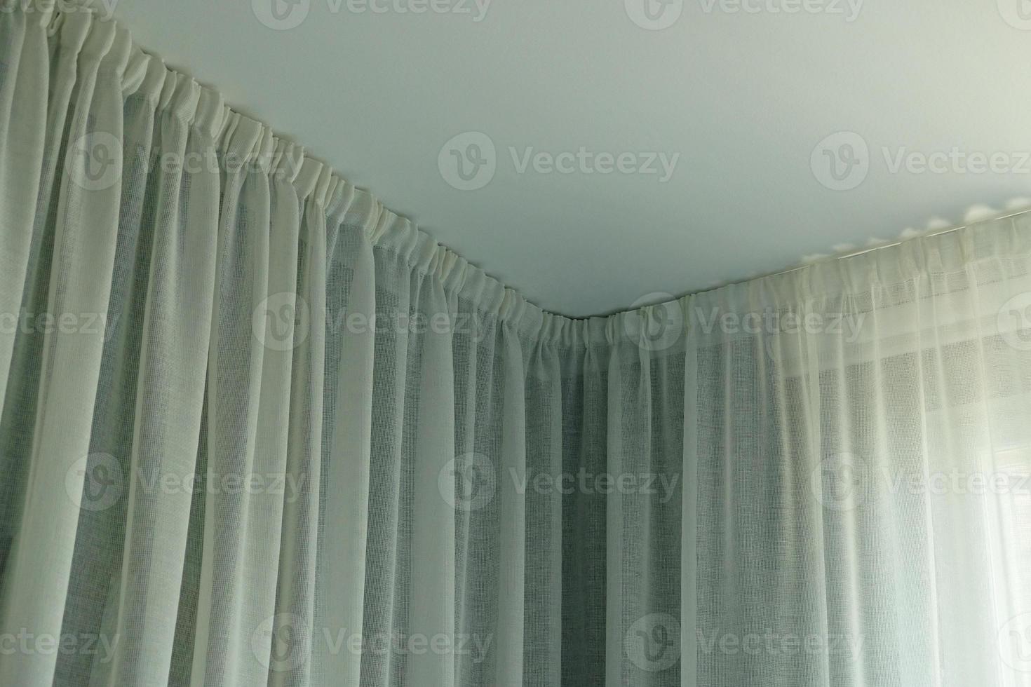 Angular cornice with drapes and white curtain or tulle. Interior details close up. White wall, ceiling, cornice niche, curtains on the window. Corner hidden curtain rod. photo