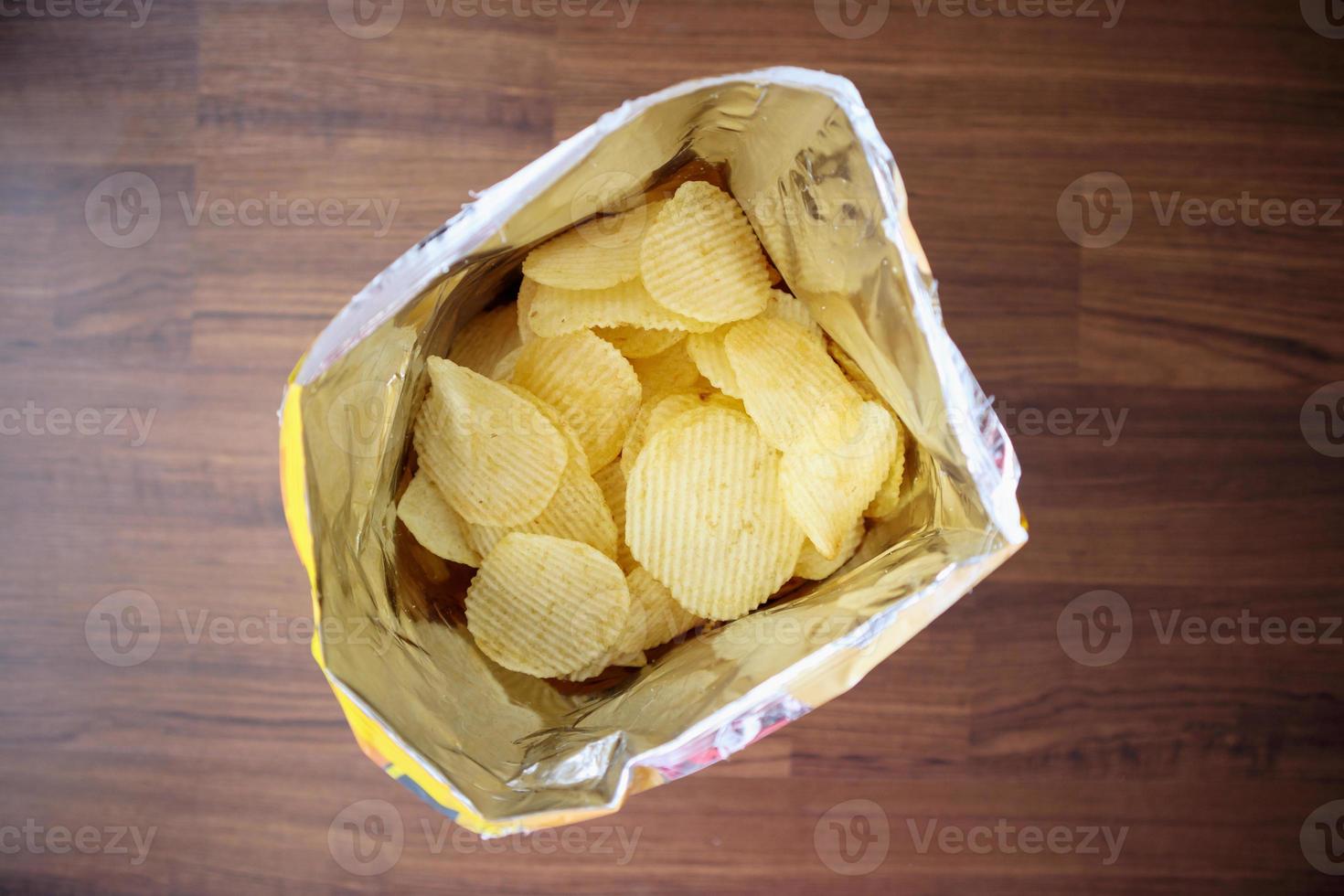 Potato chips in open snack bag close up on table floor photo