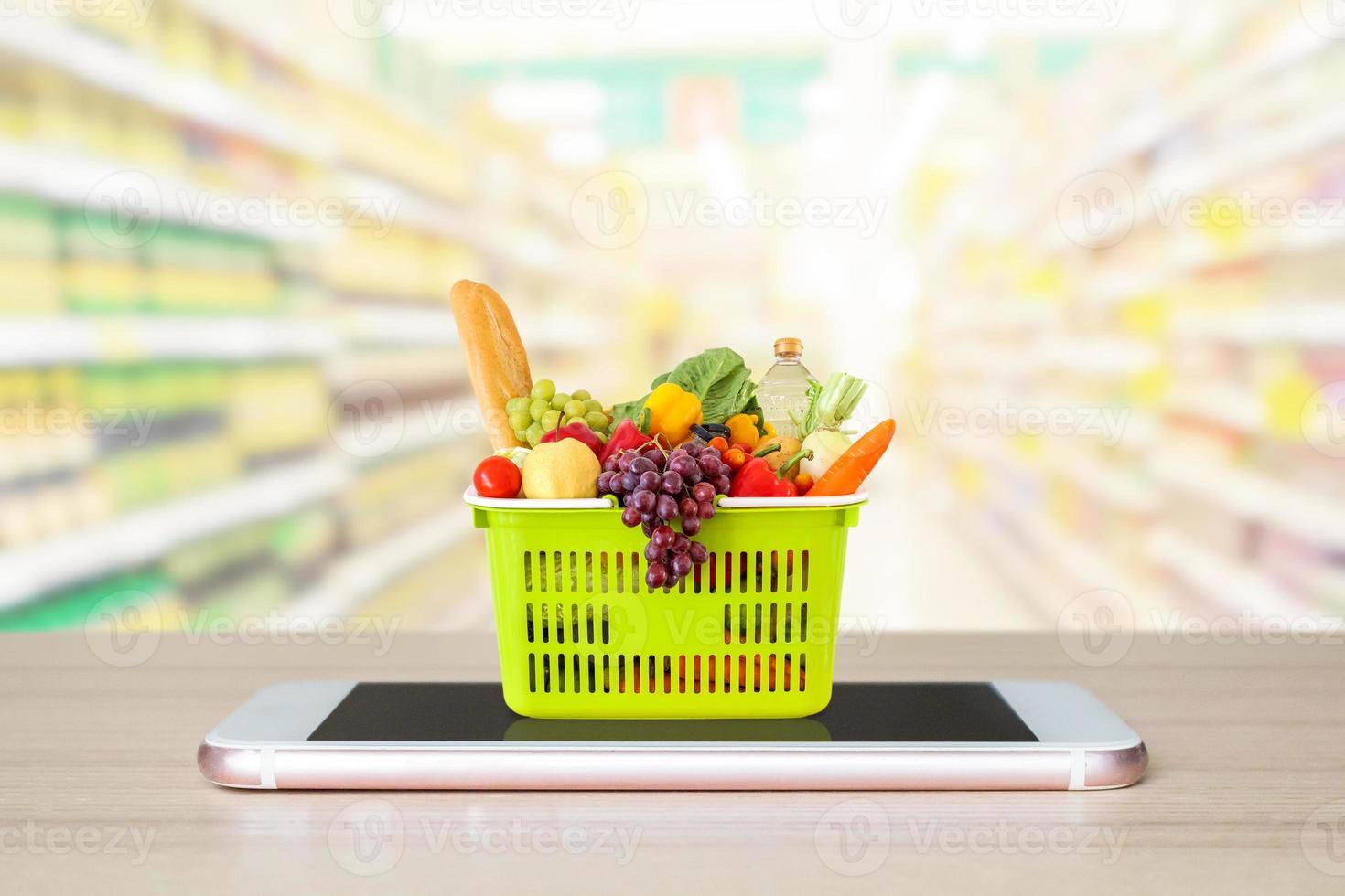 Fresh food and vegetables in shopping basket on mobile smartphone on wood table with supermarket aisle blurred background grocery online concept photo