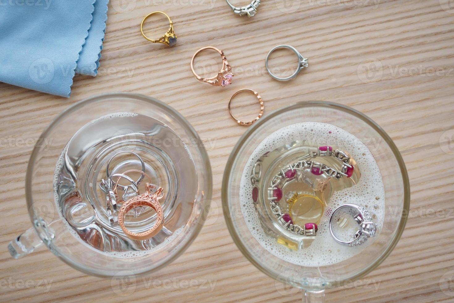 cleaning jewelry diamond ring with glass of hot water and dishwashing liquid on wood table background photo