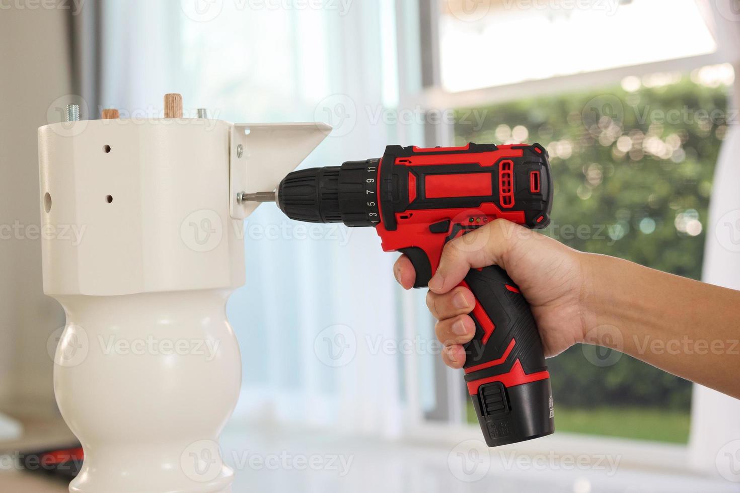 hombre montando muebles de mesa blancos en casa usando un destornillador inalámbrico foto