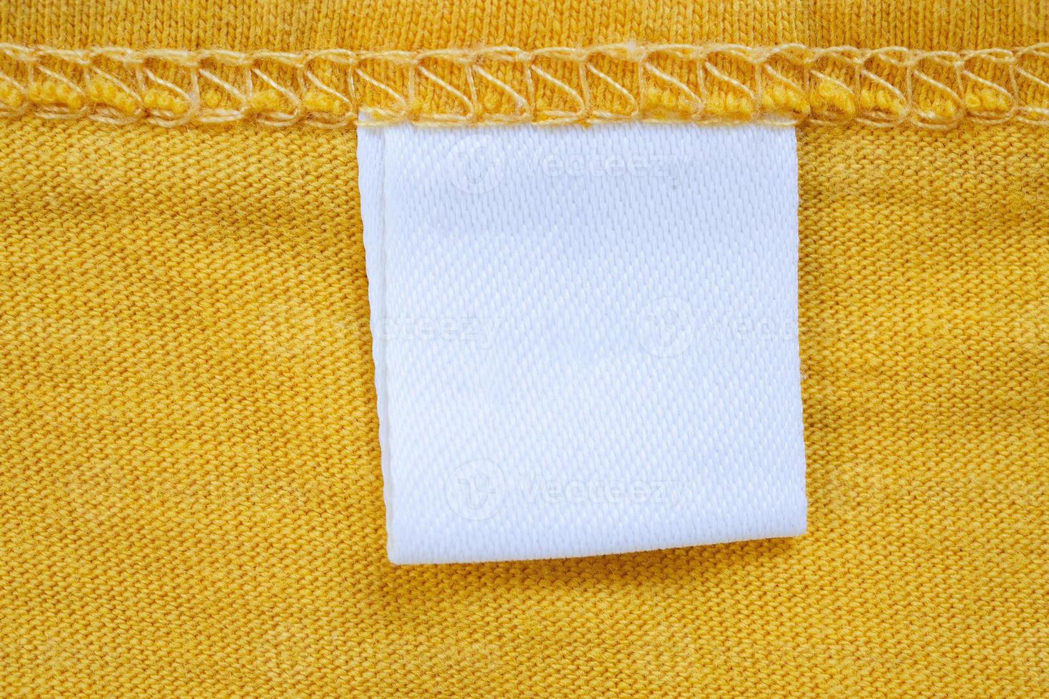 White blank clothing tag label on new yellow shirt background photo