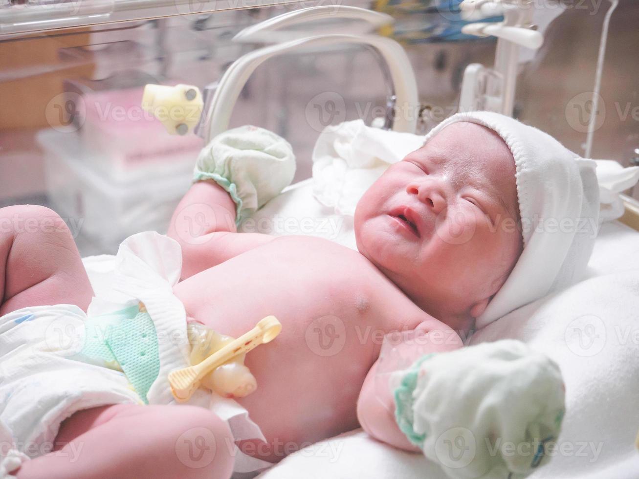 Newborn baby inside incubator in hospital post delivery room photo