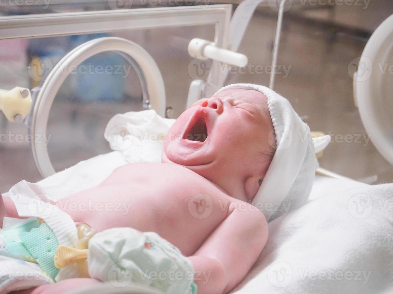 Newborn baby girl inside incubator in hospital post delivery room photo