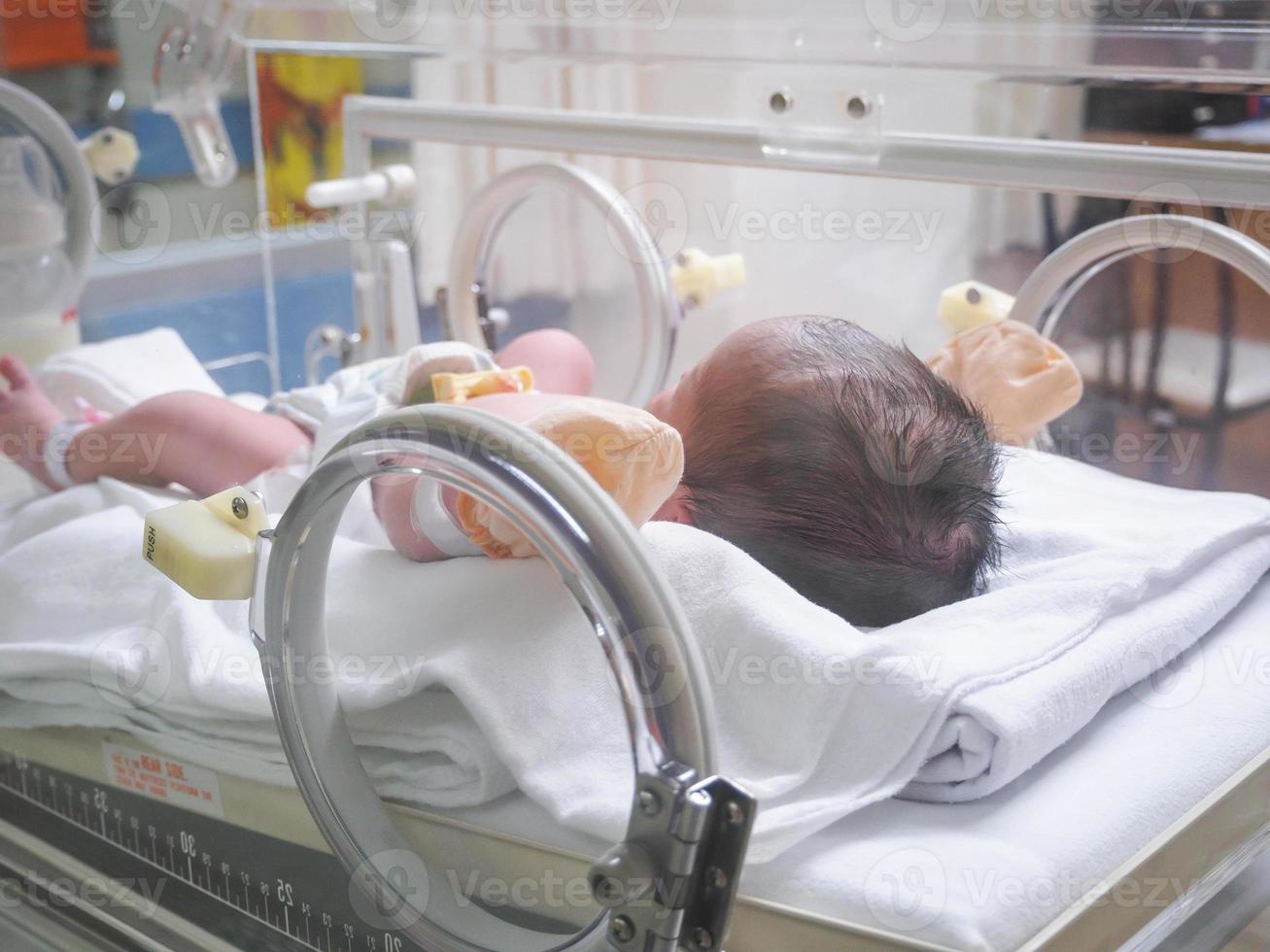 Newborn baby girl inside incubator in hospital post delivery room photo