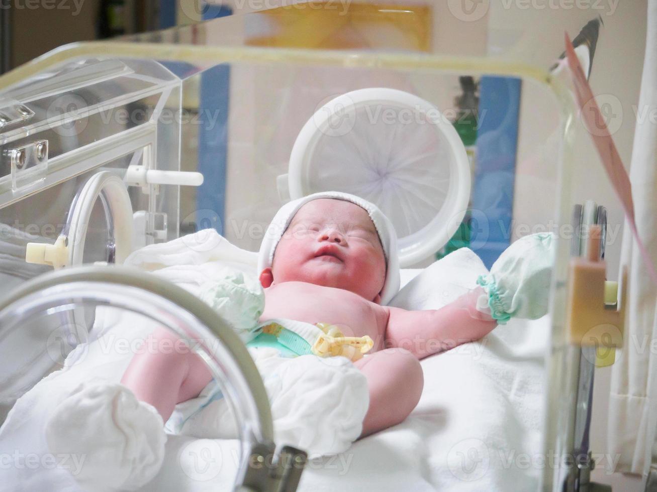 Newborn baby girl inside incubator in hospital post delivery room photo