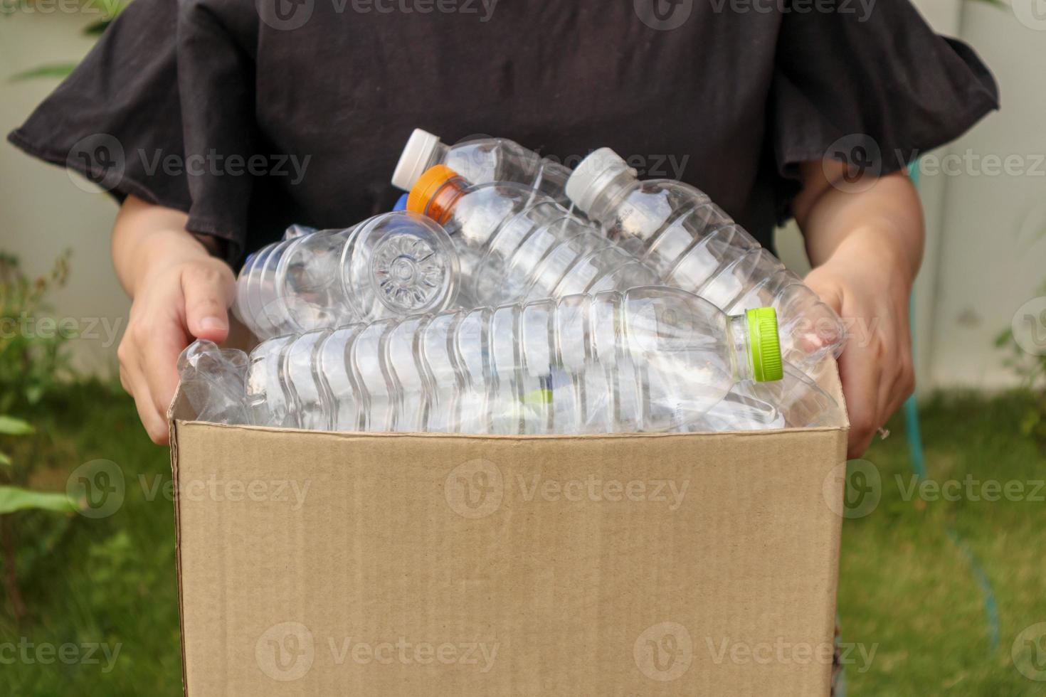 mano que sostiene la caja de basura de reciclaje marrón con botellas de plástico foto