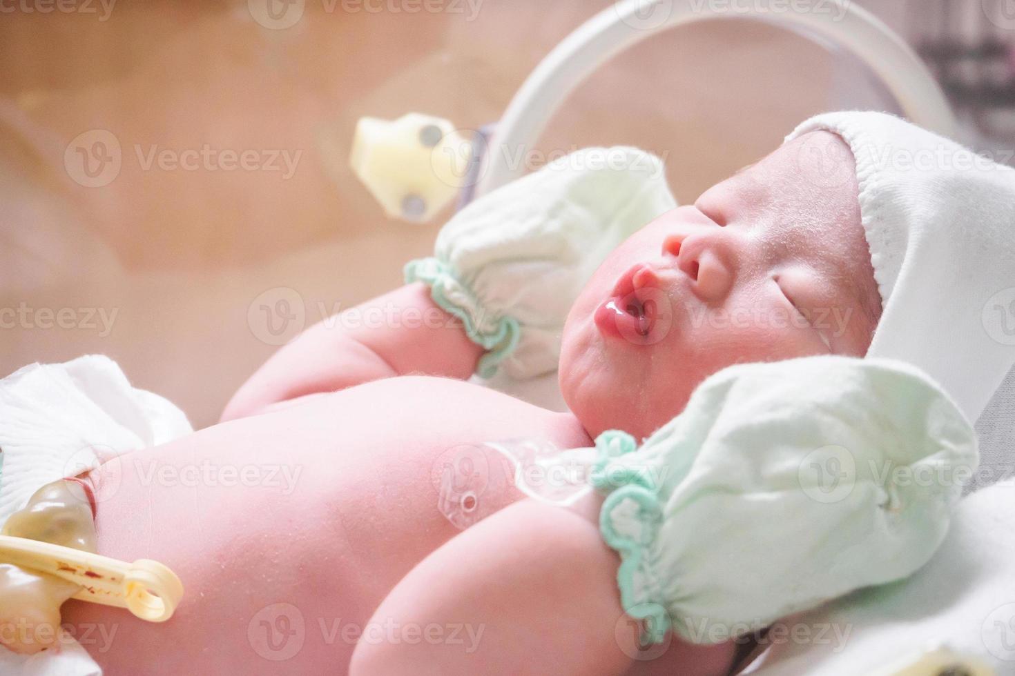 Newborn baby girl inside incubator in hospital post delivery room photo