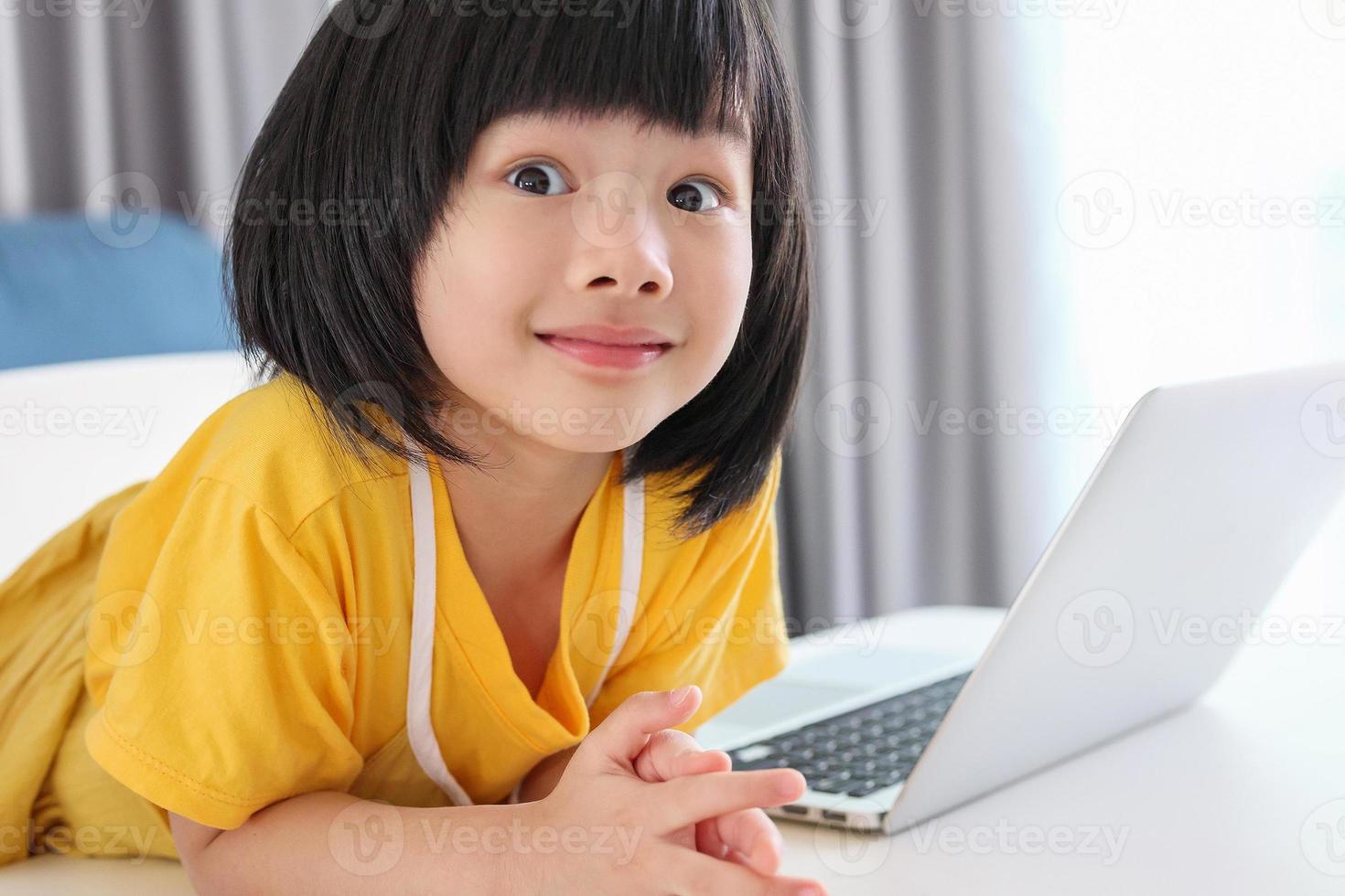little asian girl student study online using laptop computer at home photo