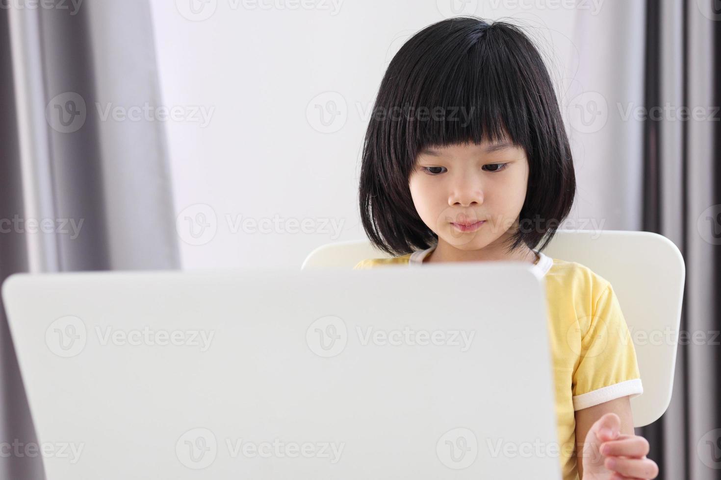 little asian girl student study online using laptop computer at home photo