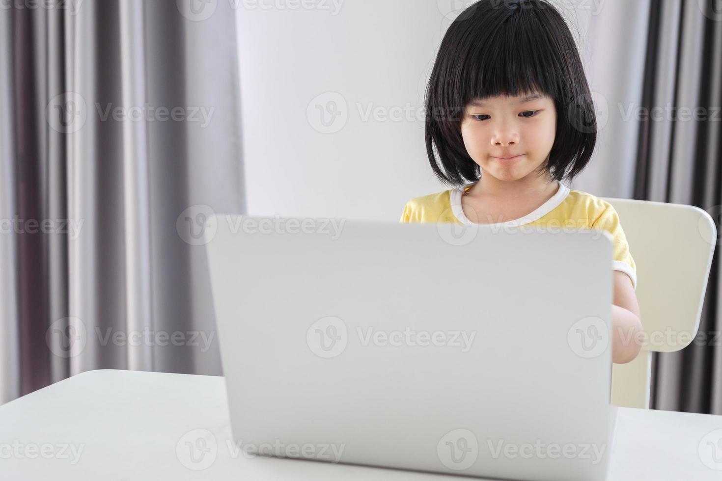 little asian girl student study online using laptop computer at home photo