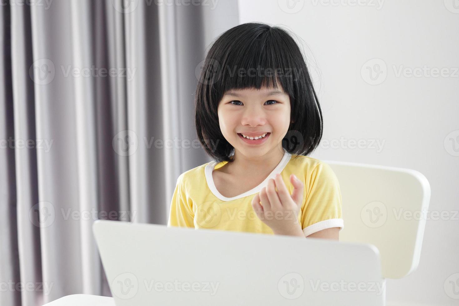 una pequeña estudiante asiática estudia en línea usando una computadora portátil en casa foto