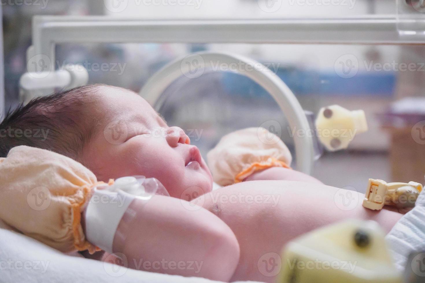 Newborn baby girl inside incubator in hospital post delivery room photo