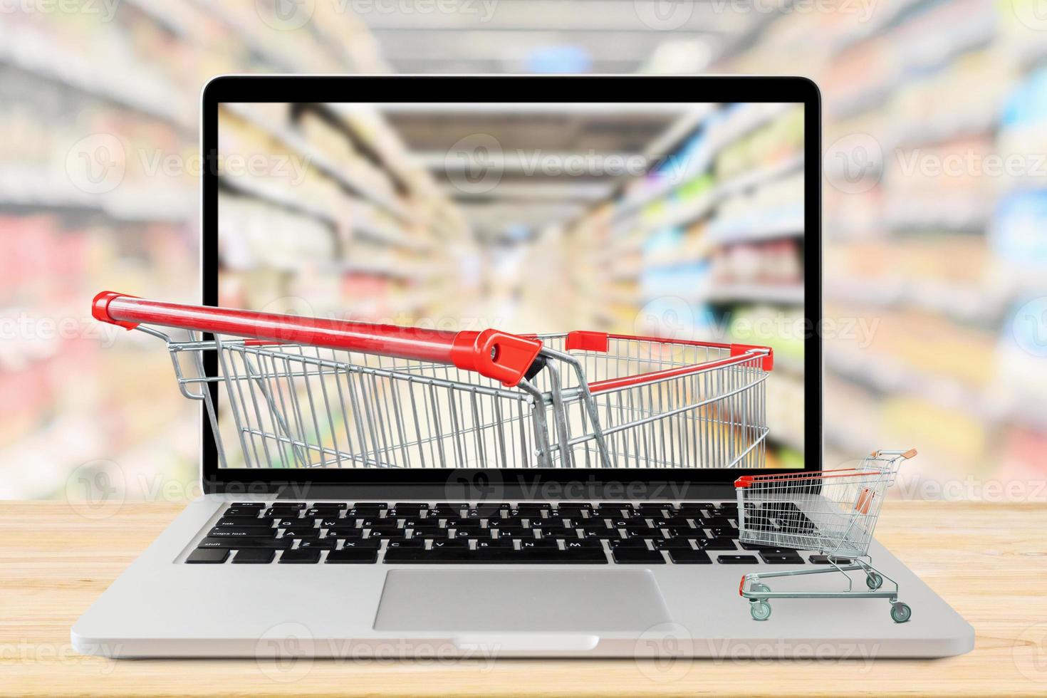 supermarket aisle blurred background with laptop computer and shopping cart on wood table grocery online concept photo