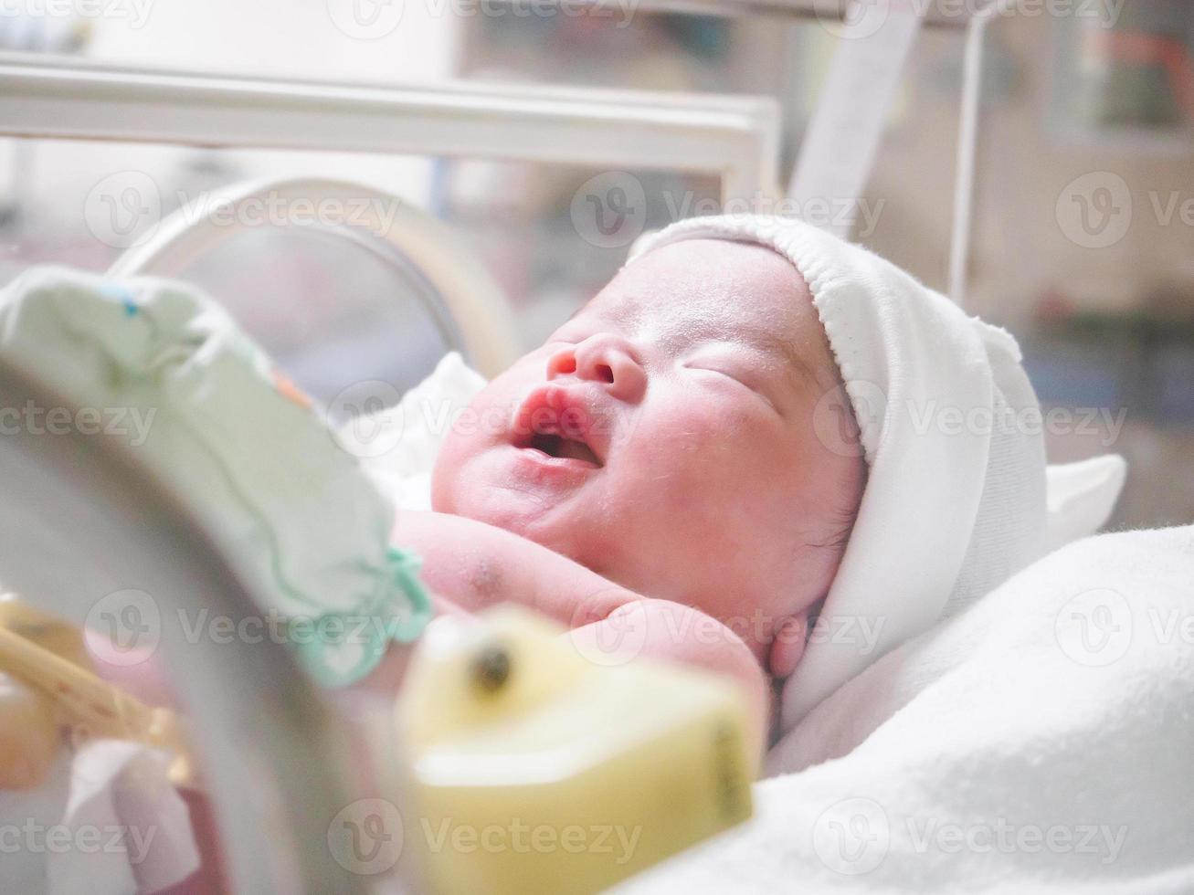 Newborn baby girl inside incubator in hospital post delivery room photo