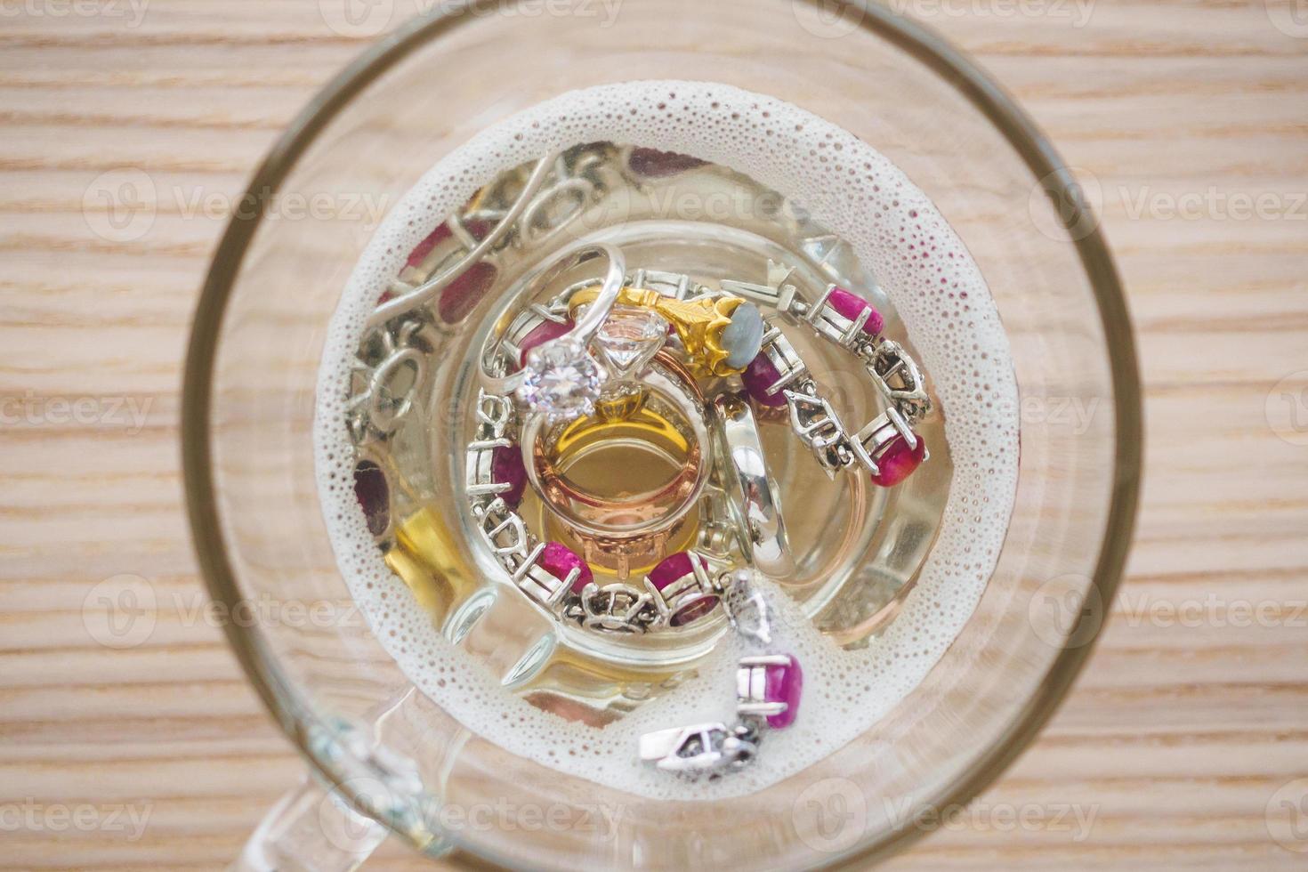 cleaning vintage jewelry diamond ring and bracelet in glass on wood table background photo