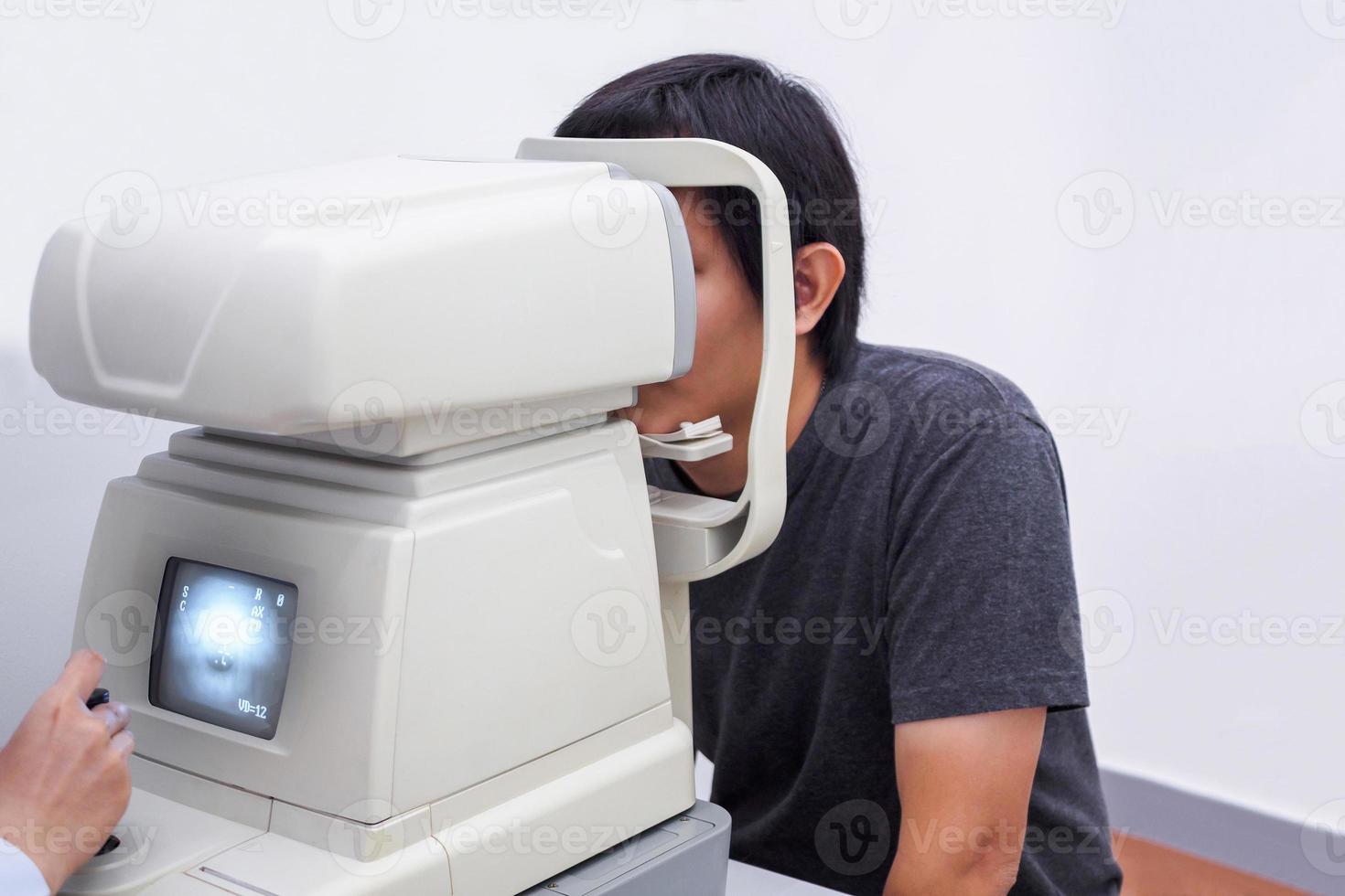 Young handsome asian man take eye exam with optical eye test machine photo