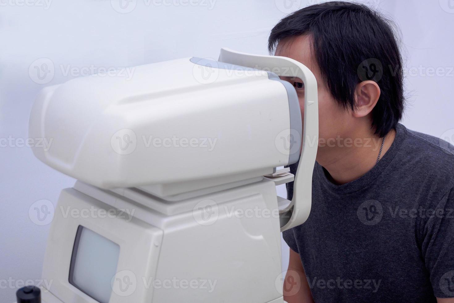 Young handsome asian man take eye exam with optical eye test machine photo