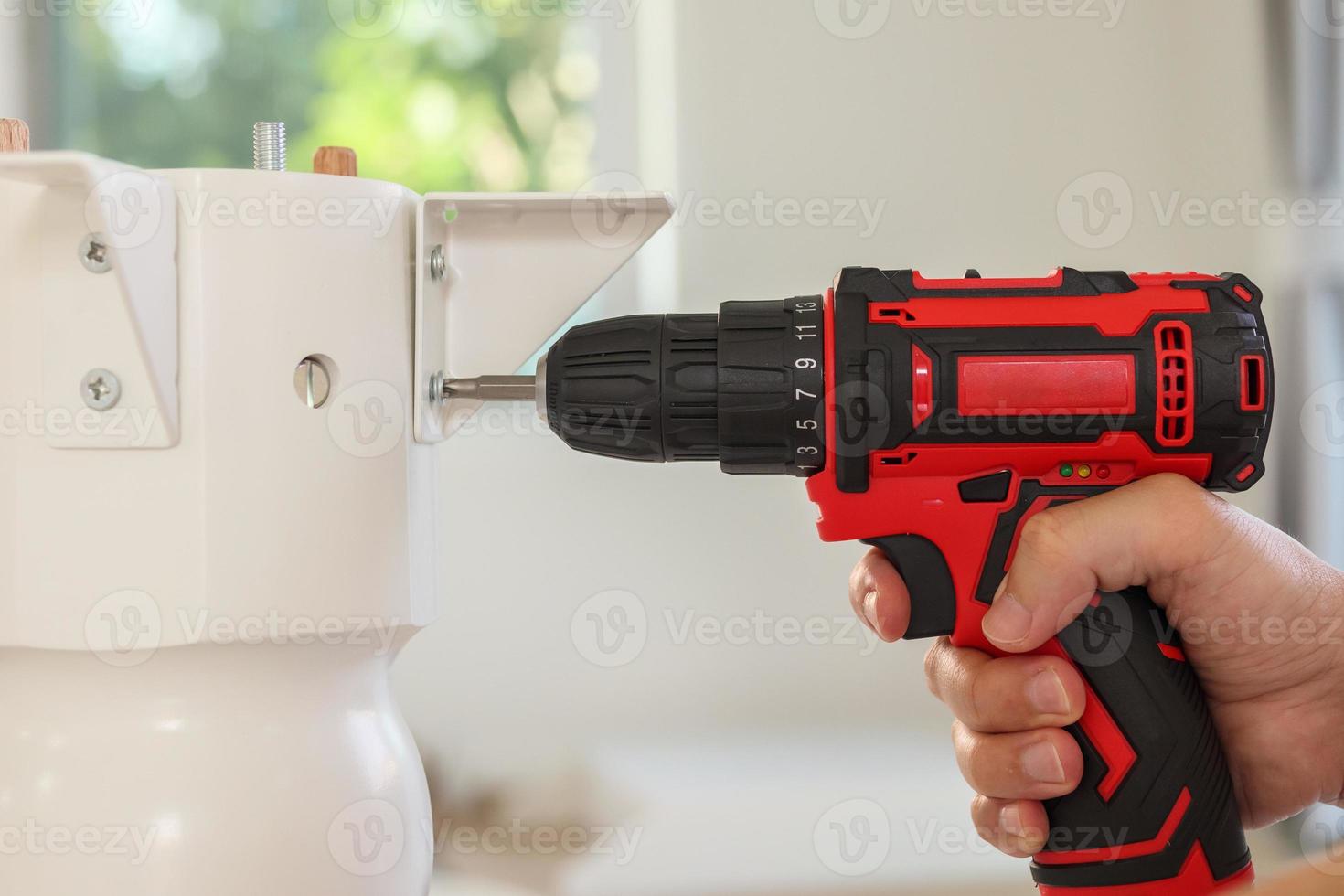 man assembling white table furniture at home using cordless screwdriver photo