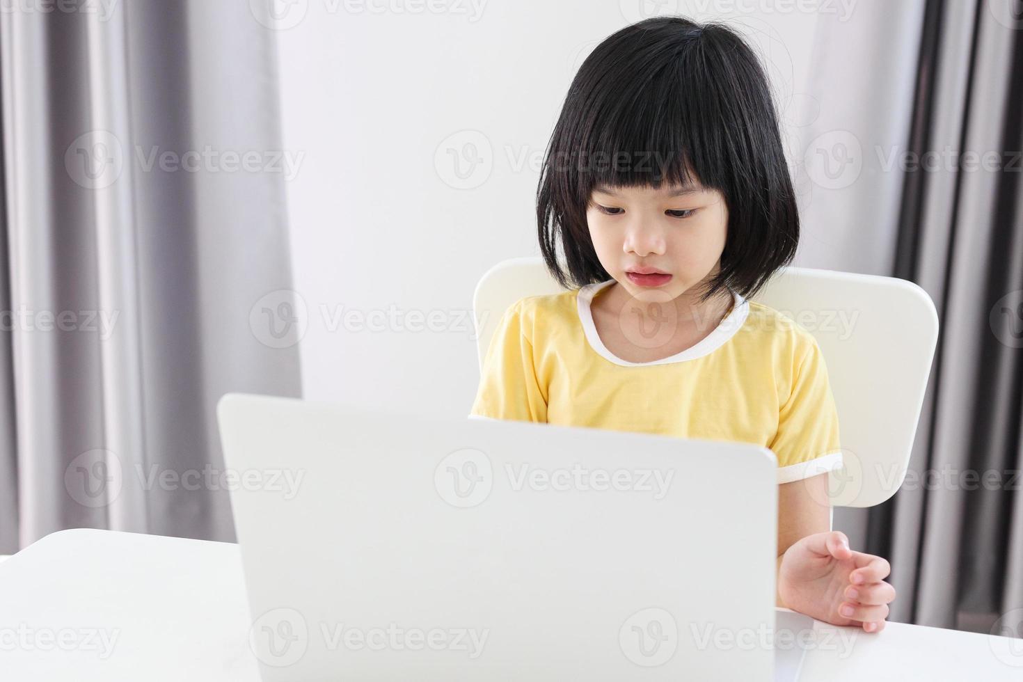 little asian girl student study online using laptop computer at home photo