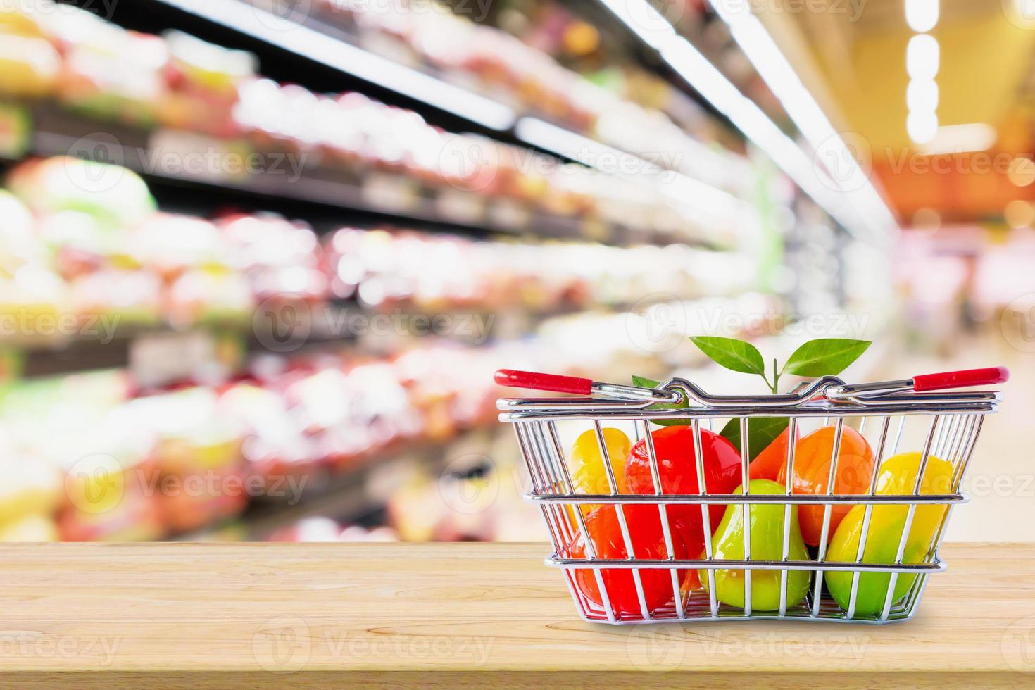 Shopping basket with fruit on wood table over grocery store supermarket blur background photo