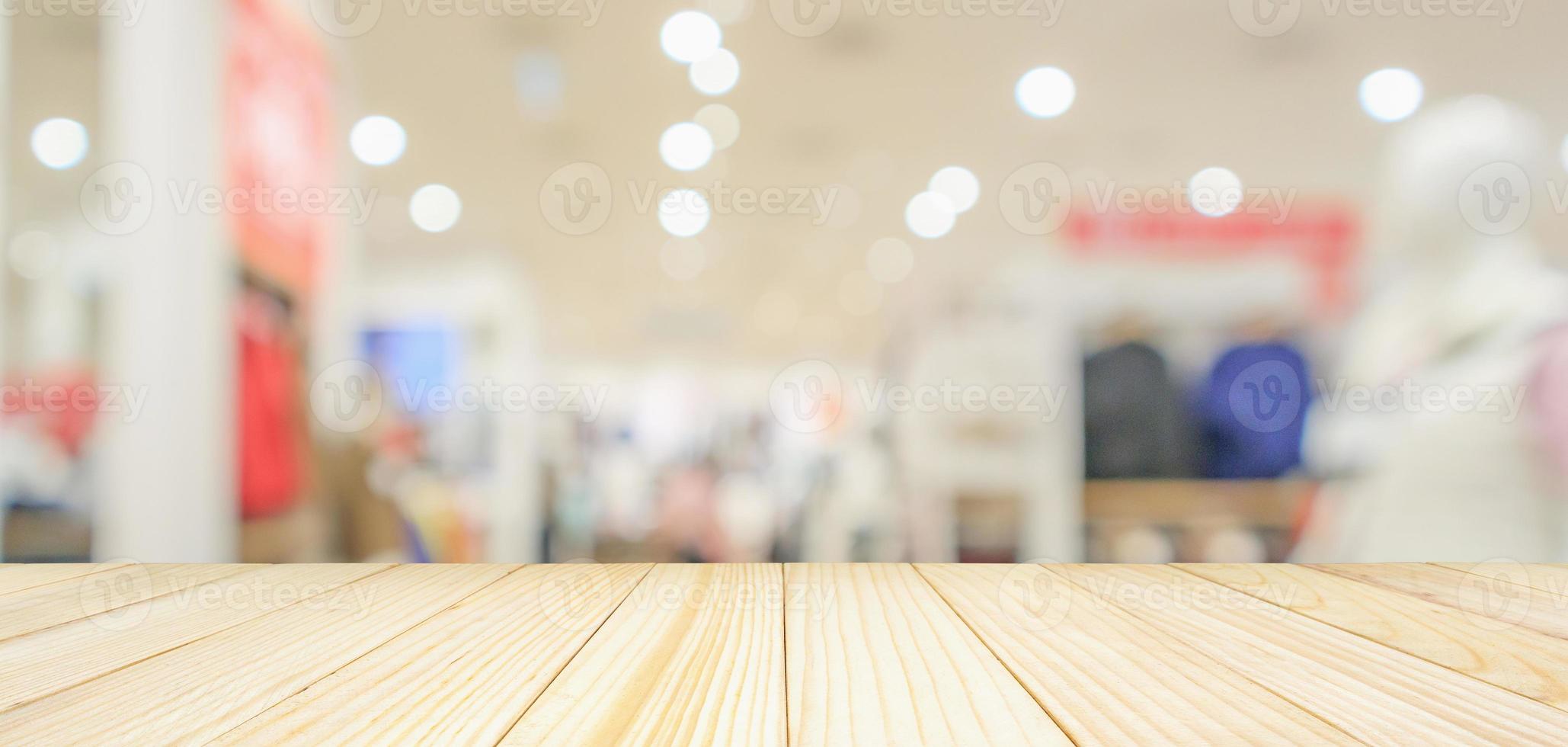 Empty wood table top with modern clothing store interior blur abstract defocused background with bokeh light for product display photo