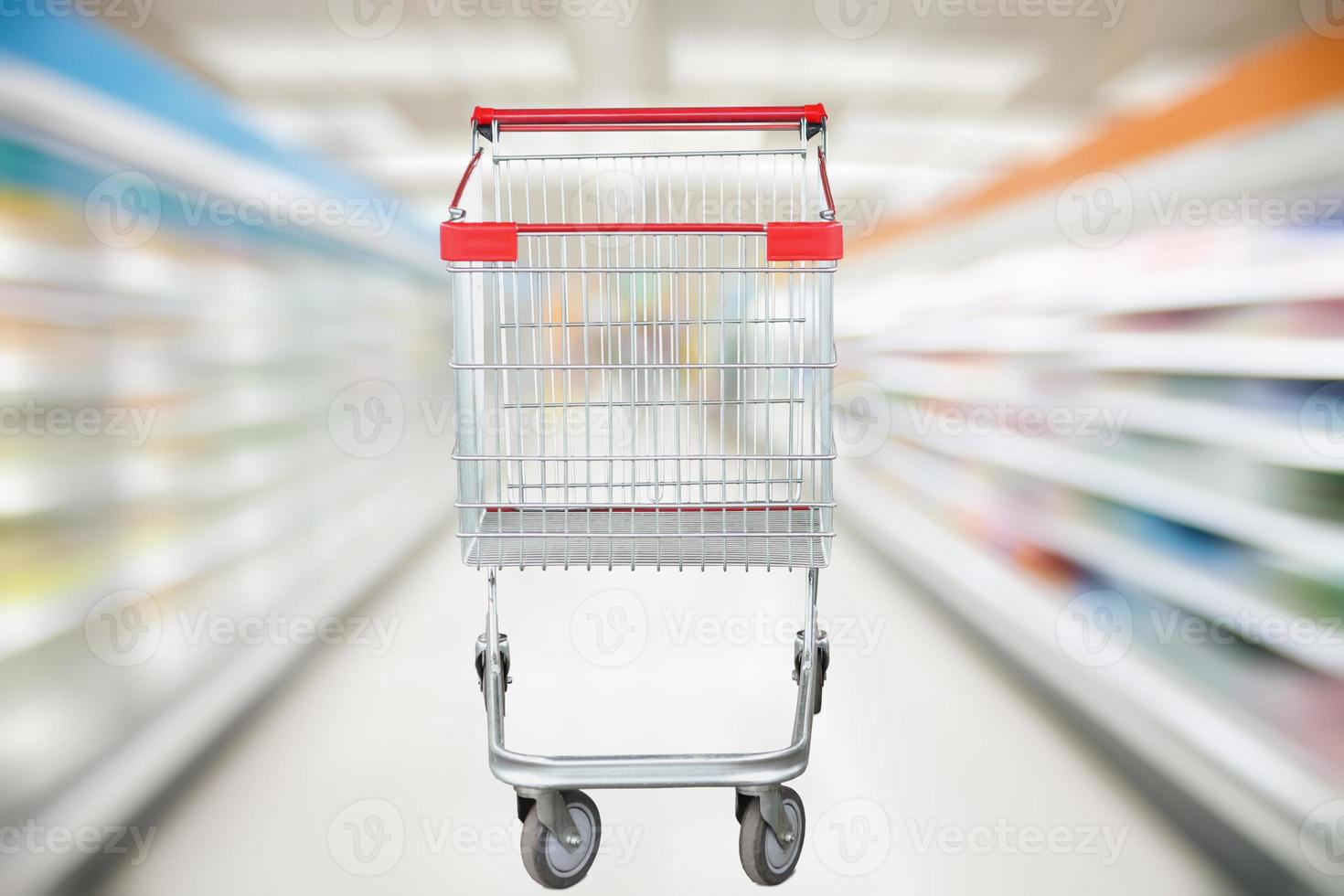 Supermarket aisle blur defocused background with empty red shopping cart photo