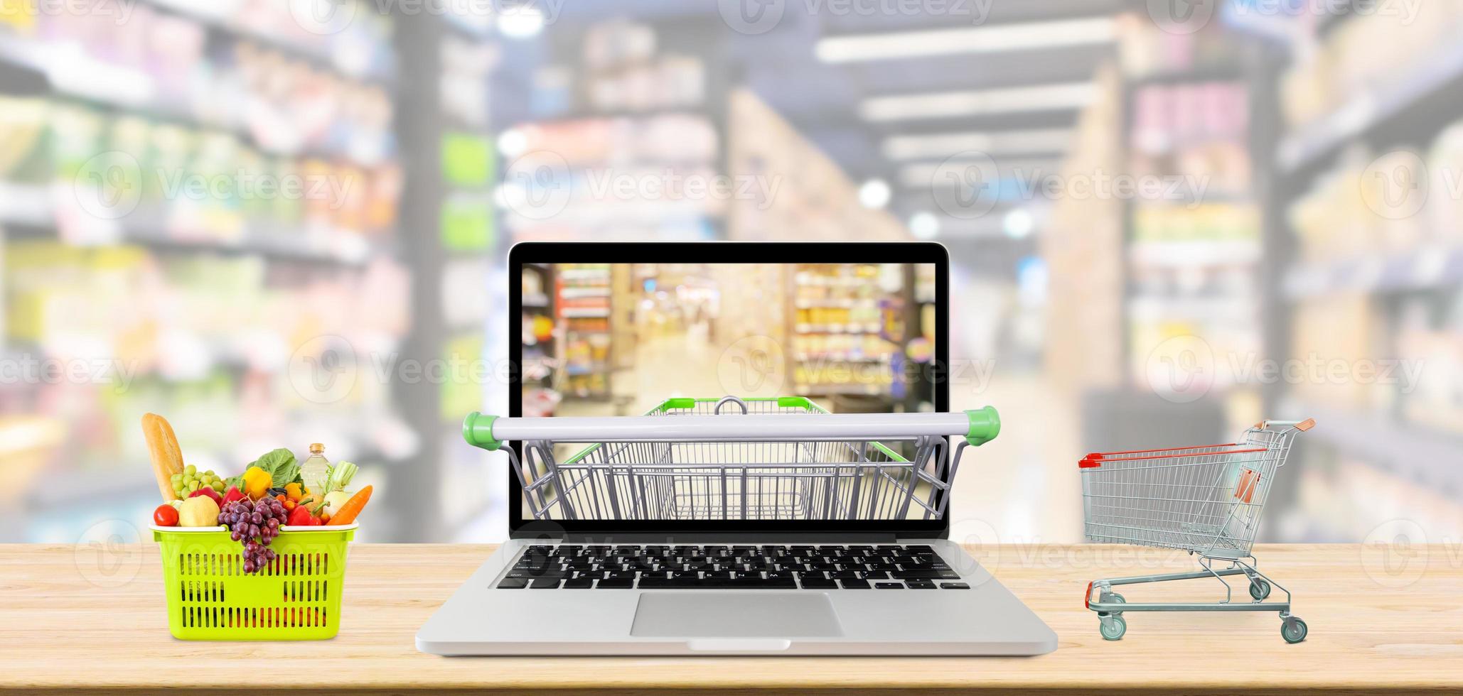 supermarket aisle blurred background with laptop computer and shopping cart on wood table grocery online concept photo