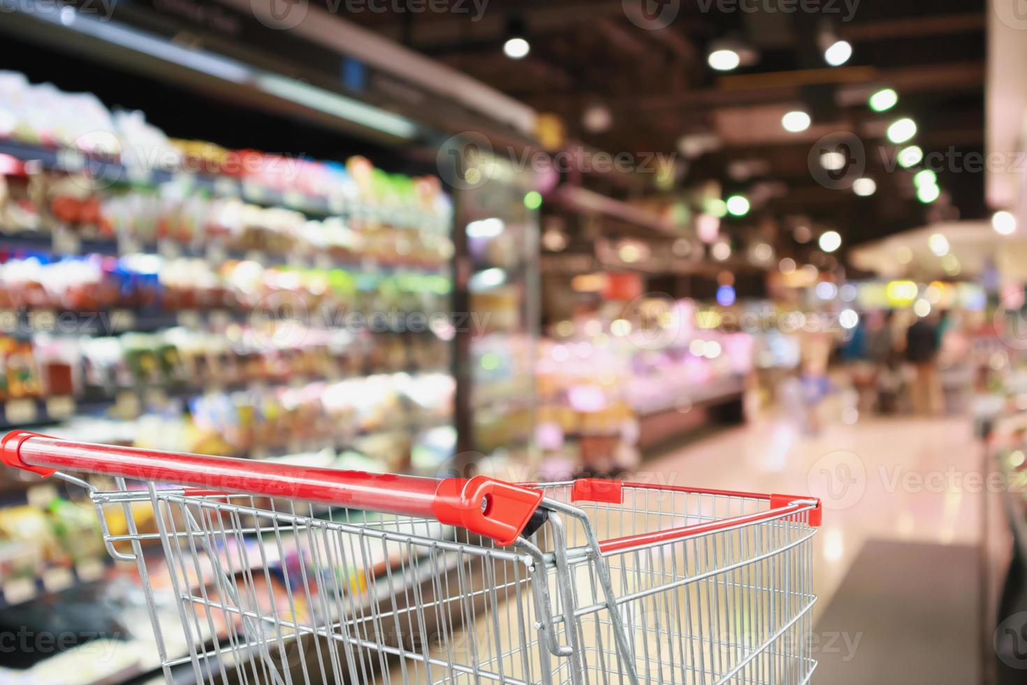 supermarket grocery store with fruit and vegetable shelves interior defocused background with empty red shopping cart photo