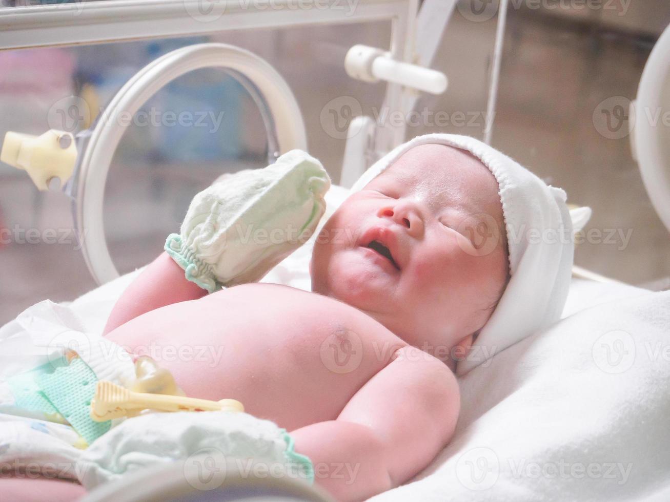 Newborn baby girl inside incubator in hospital post delivery room photo