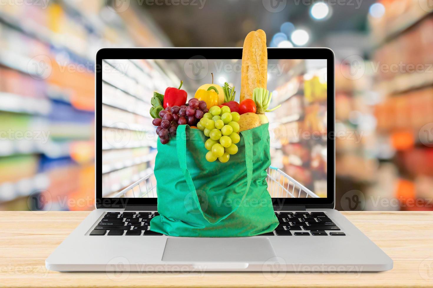 supermarket aisle blurred background with laptop computer and green shopping bag on wood table grocery online concept photo