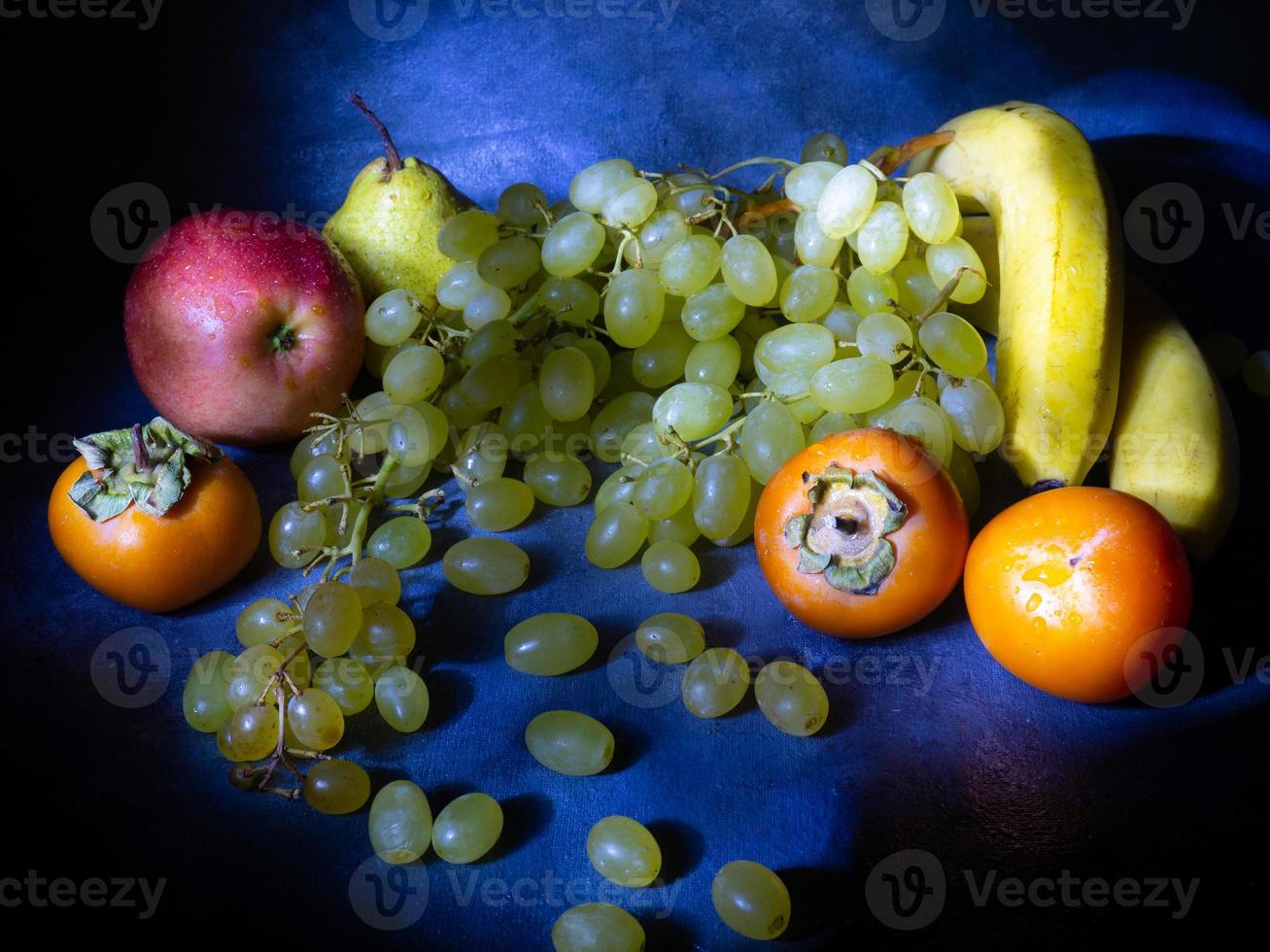Bodegón de frutas. manzana, caqui, pera y uvas sobre un fondo negro. manzanilla caqui. gala de manzana pera lucas. alimentación saludable. vegetarianismo foto