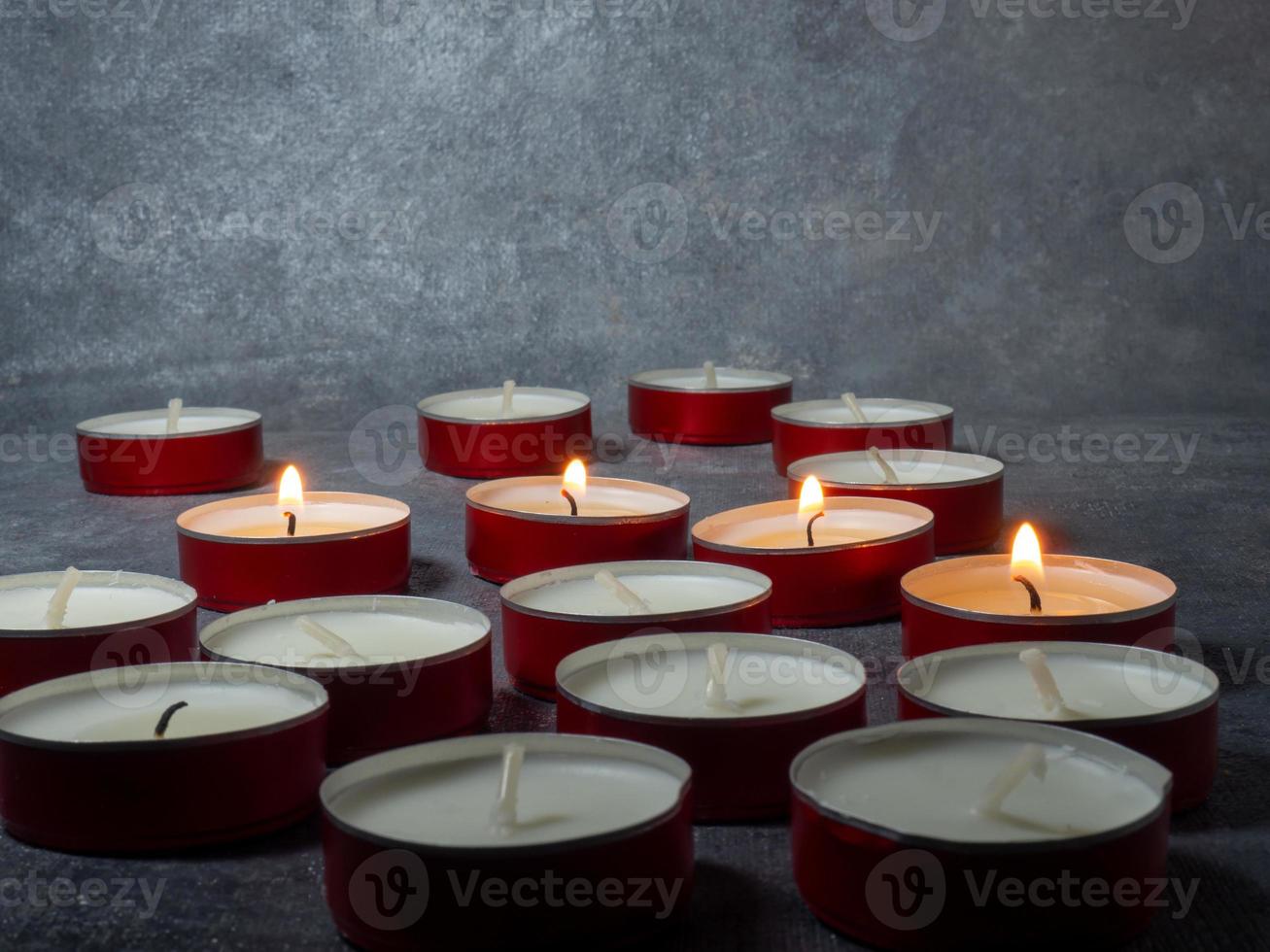 Short candles are burning against a dark background. Lots of small candles. Not all candles are lit. photo