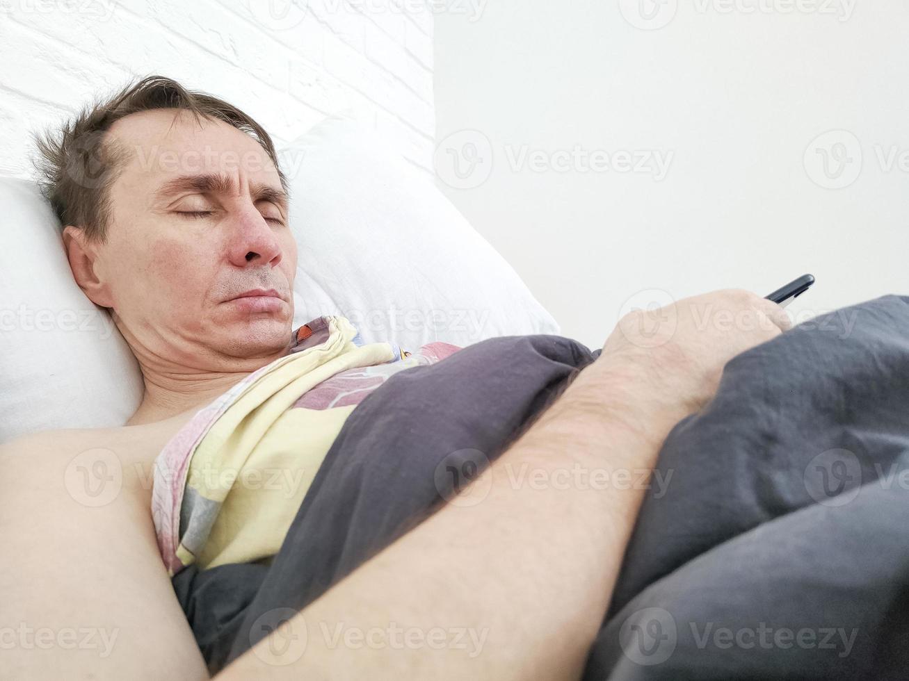 Man sleeping in bed with phone in his hands photo
