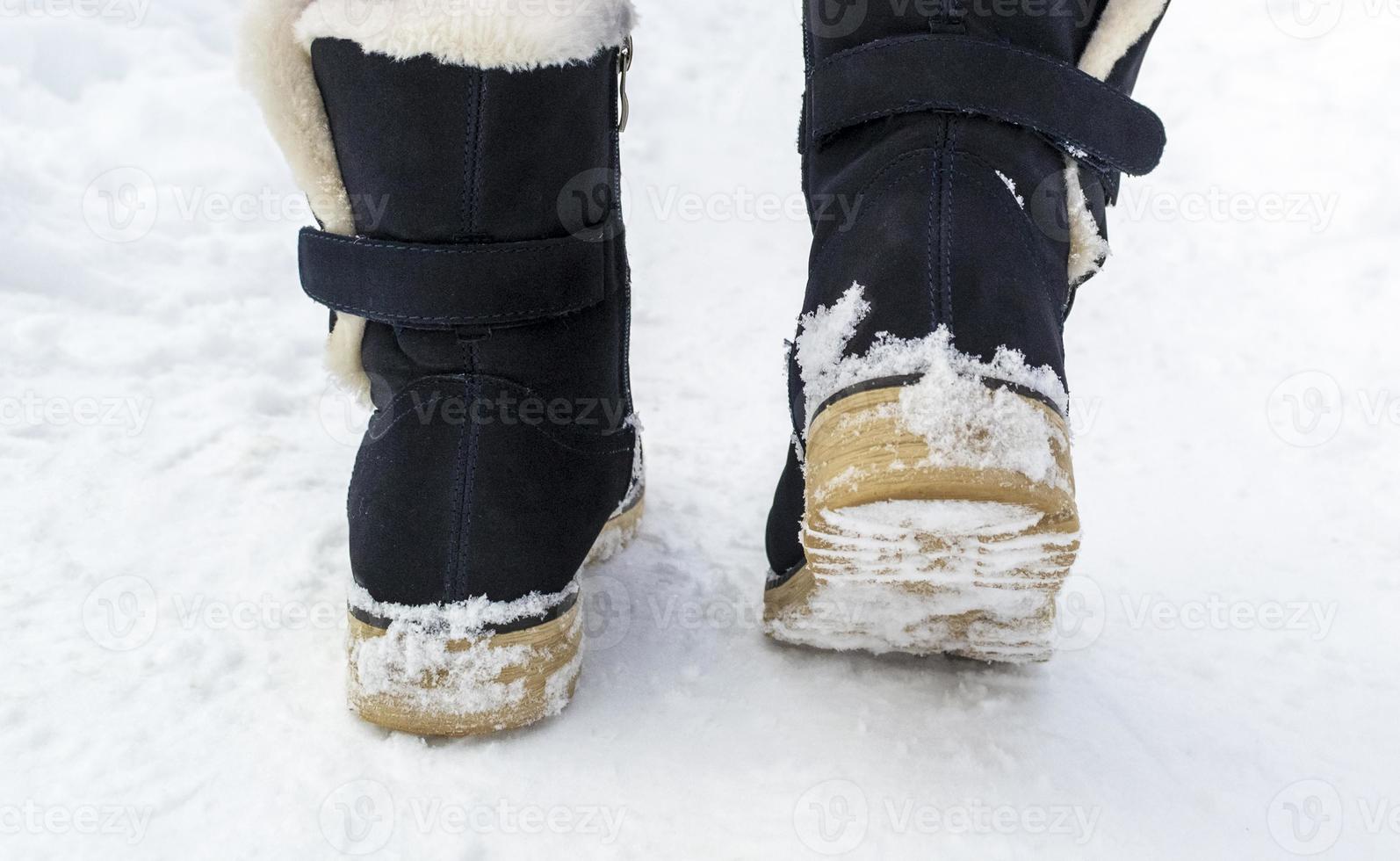 Female feet in black boots walking in winter snow photo