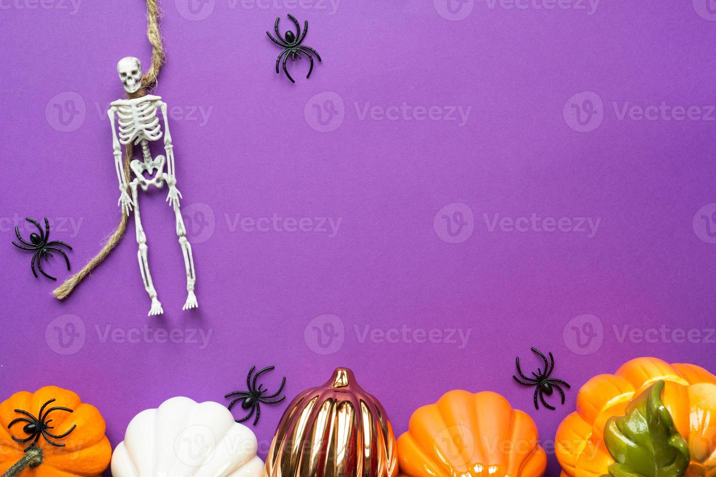 Halloween layout of garland of skeleton on a rope, glowing Jack o Lantern, pumpkins, spiders on a purple background. Flat lay horror and a terrible holiday photo