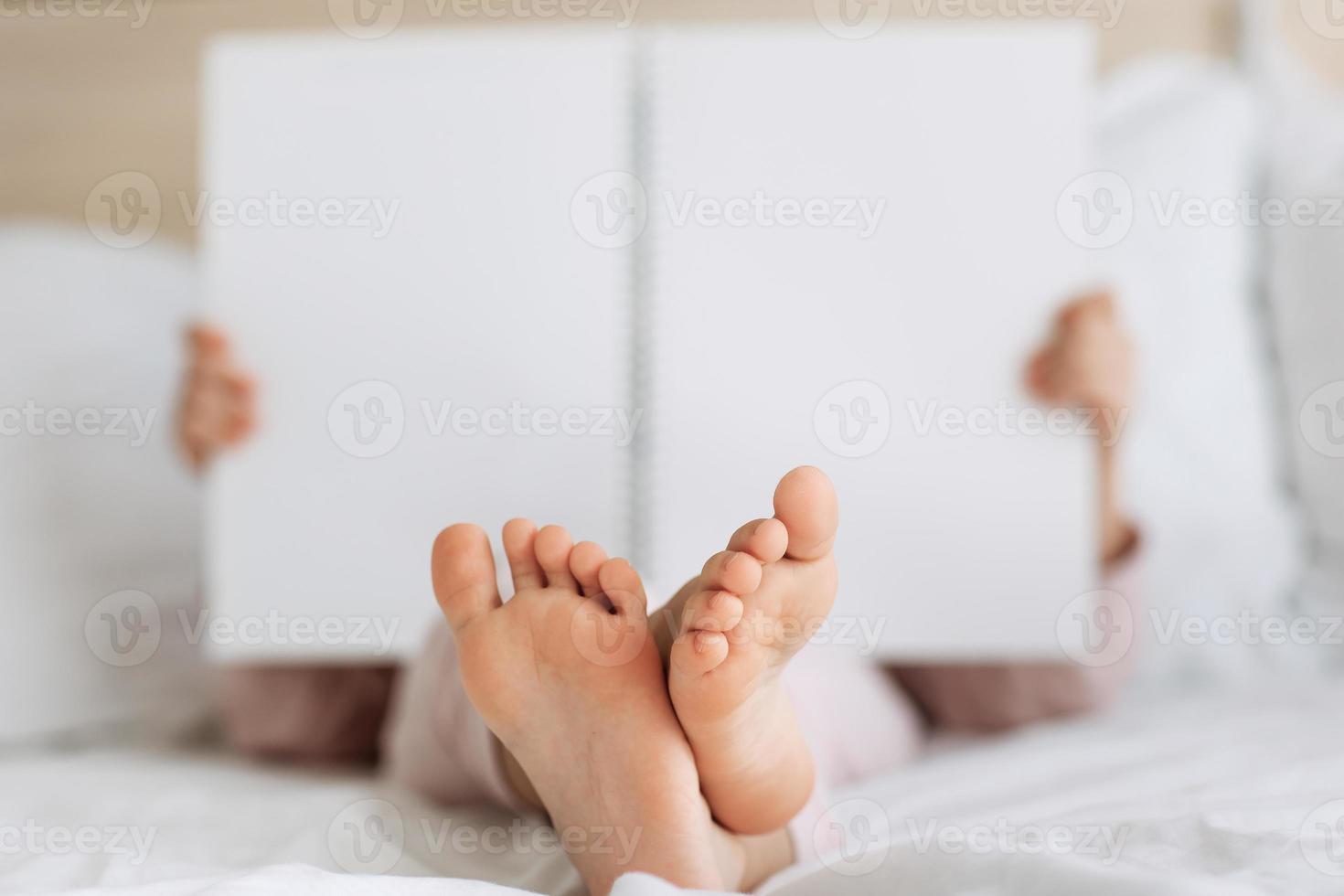 Children bare feet and hands close up Kid reading book in white cozy bed before sleepping night Copy space mock up place for text Rest and holiday in hotel photo