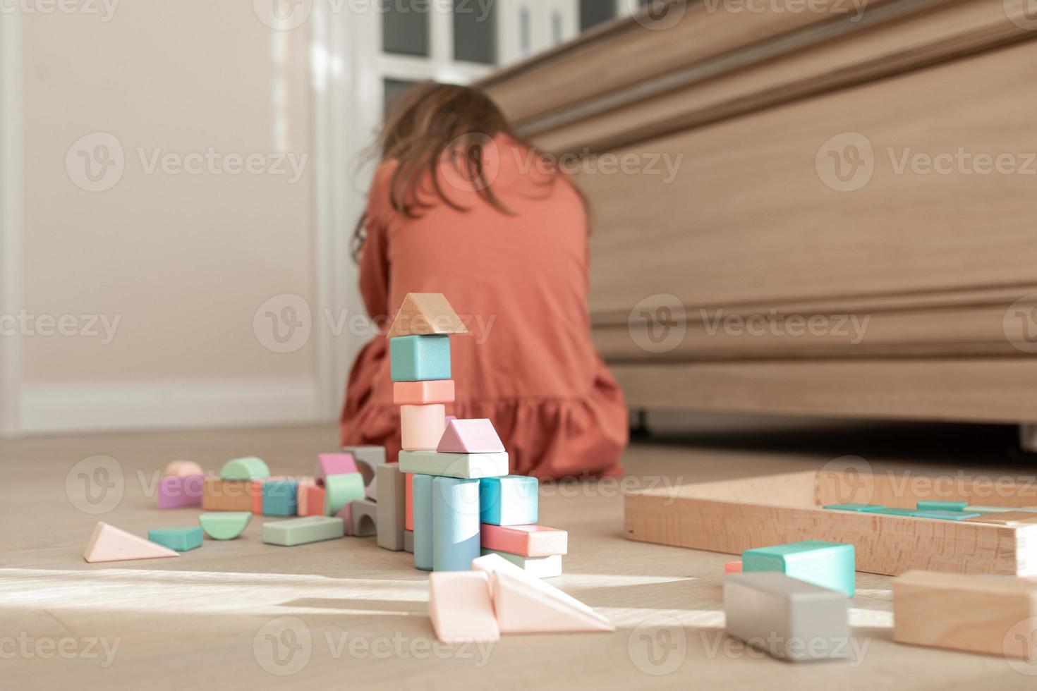 la niña está sentada dando la vuelta al suelo en la habitación con tiys de madera y llorando foto