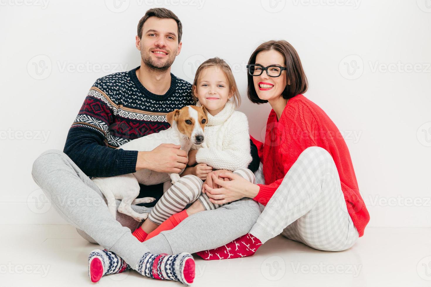 una foto aislada de una mujer y un hombre de buen aspecto se sientan junto con su hija y el perro jack russell terrier, se abrazan, aislados en un fondo blanco. concepto de familia y unión