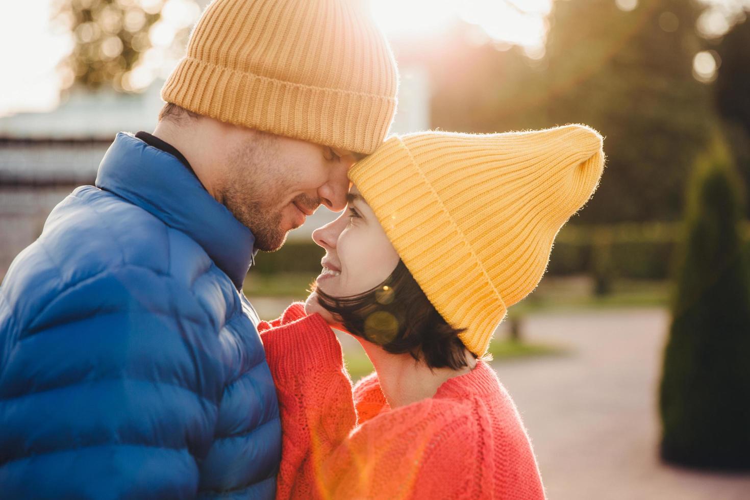 Romantic young couple look at each other with great love, have nice relationship, going to kiss, have walk outdoor in park, wear warm clothes. Lovely couple with eyes full of love and smile. photo