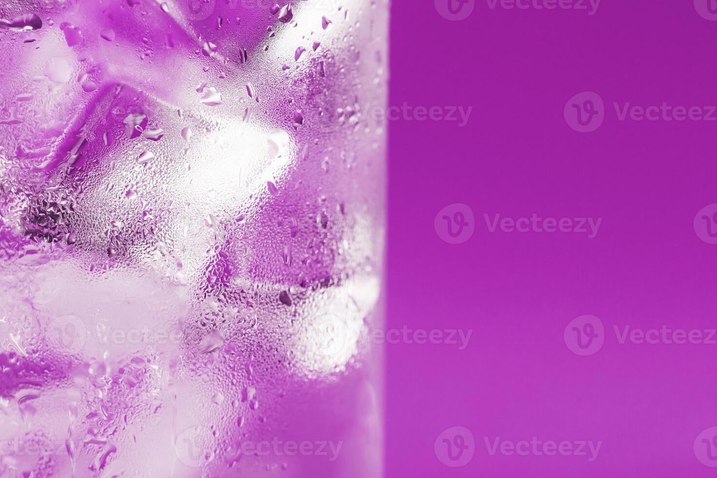 Ice cubes in a glass with refreshing ice water on a pink background