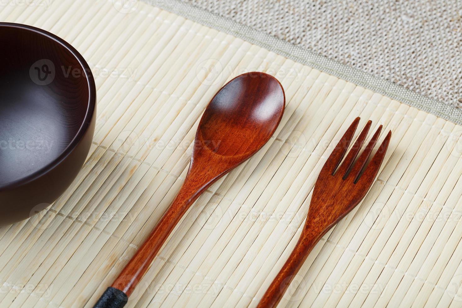 Empty dark wooden cup, spoon and fork made of natural wood on a light bamboo backing photo