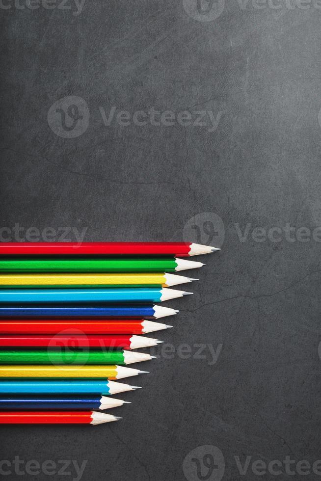 lápices multicolores para dibujar y dibujar en fila sobre un fondo negro texturizado en fila foto