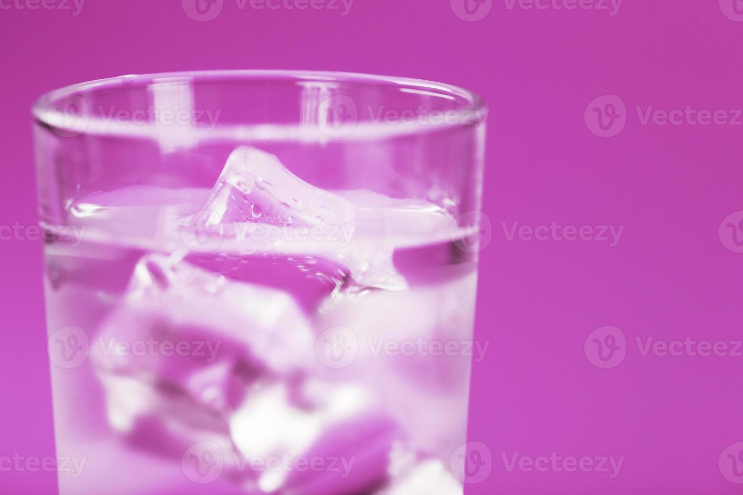 vaso con agua y cubitos de hielo sobre un fondo rosa foto