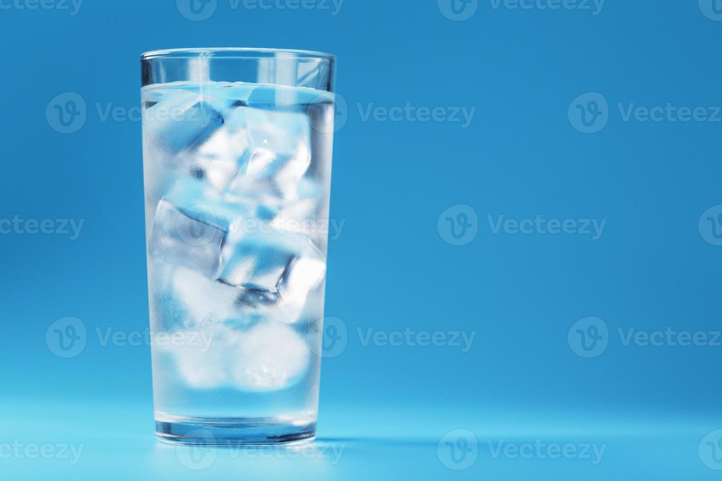 vaso con agua y cubitos de hielo sobre un fondo azul foto